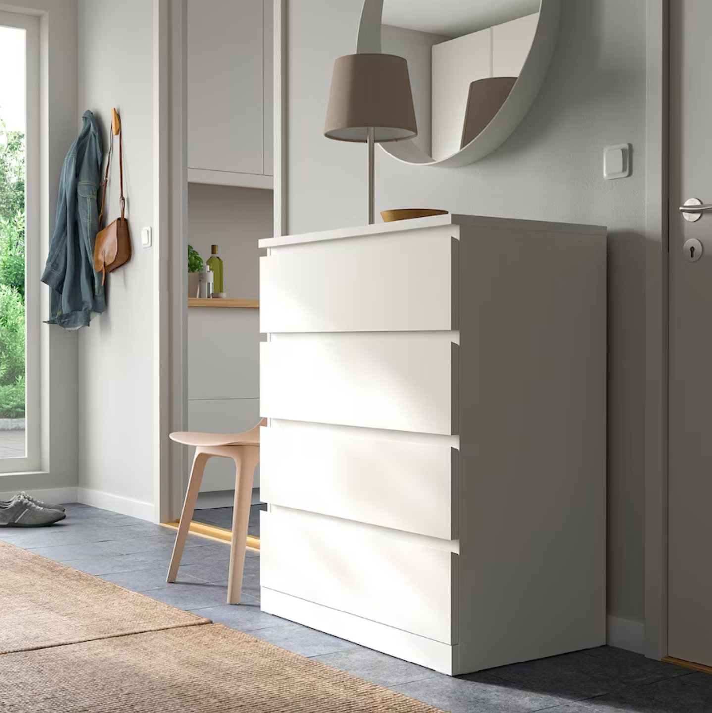 A white MALM chest of 4 drawers, 80x100 cm, placed in a room setting with a stool in front and a coat hanging on the wall in the background.