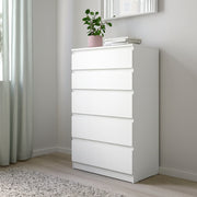 White dresser with a plant and books in a room with light gray walls and curtains.