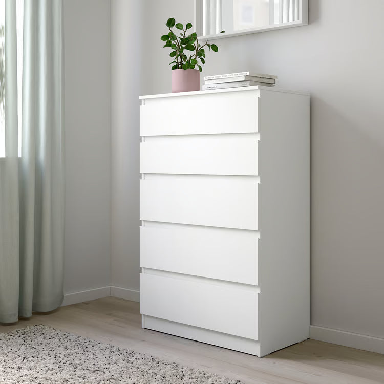 White dresser with a plant and books in a room with light gray walls and curtains.