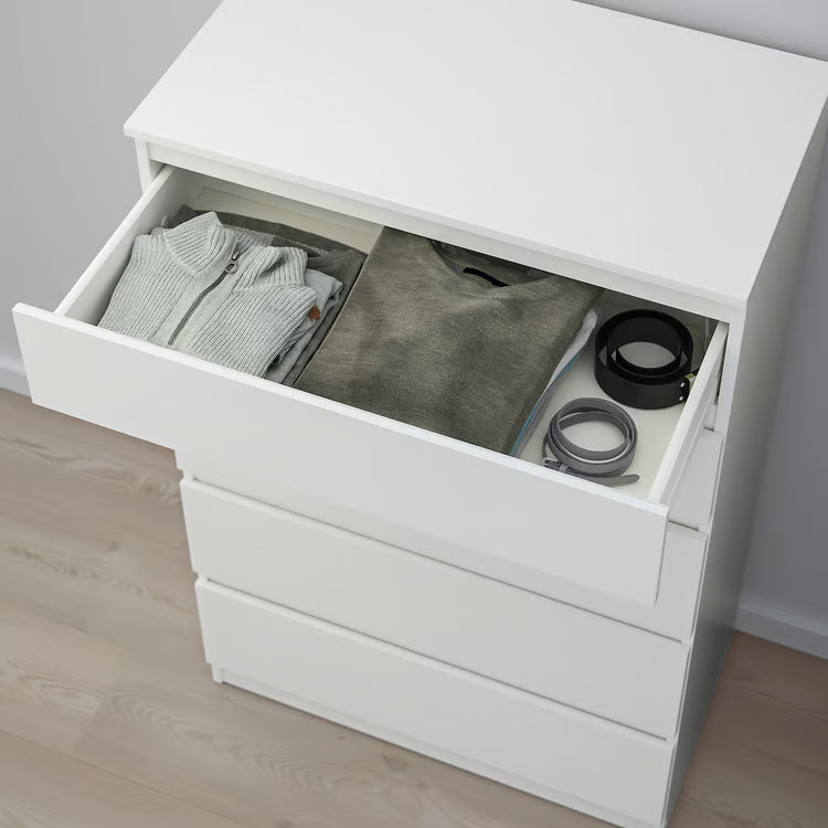White dresser with open drawer containing clothes and a black item on a wooden floor.